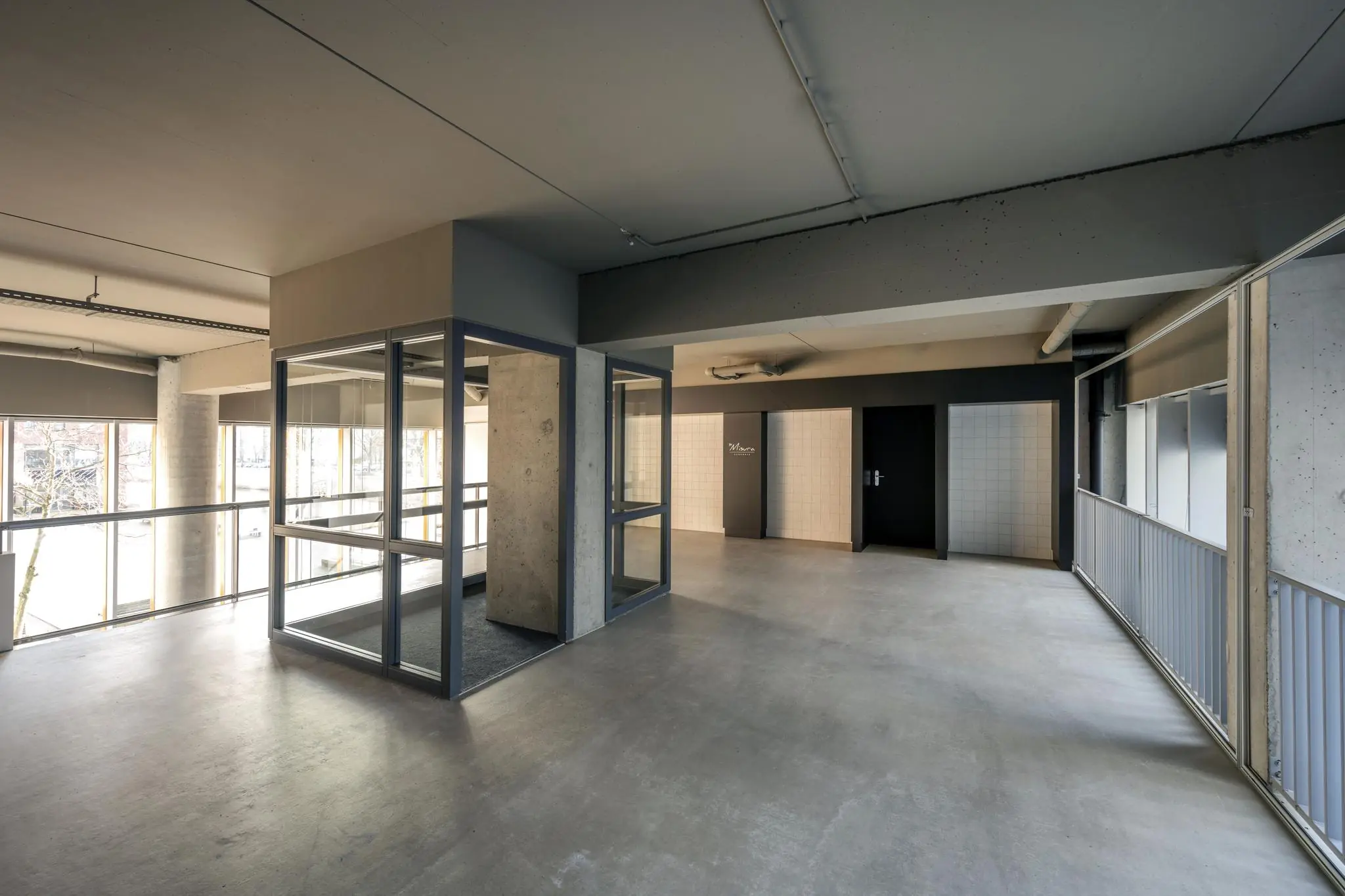 Lichte, moderne hal met glazen lift en betonnen afwerking in een gebouw aan het George Gershwinplein.